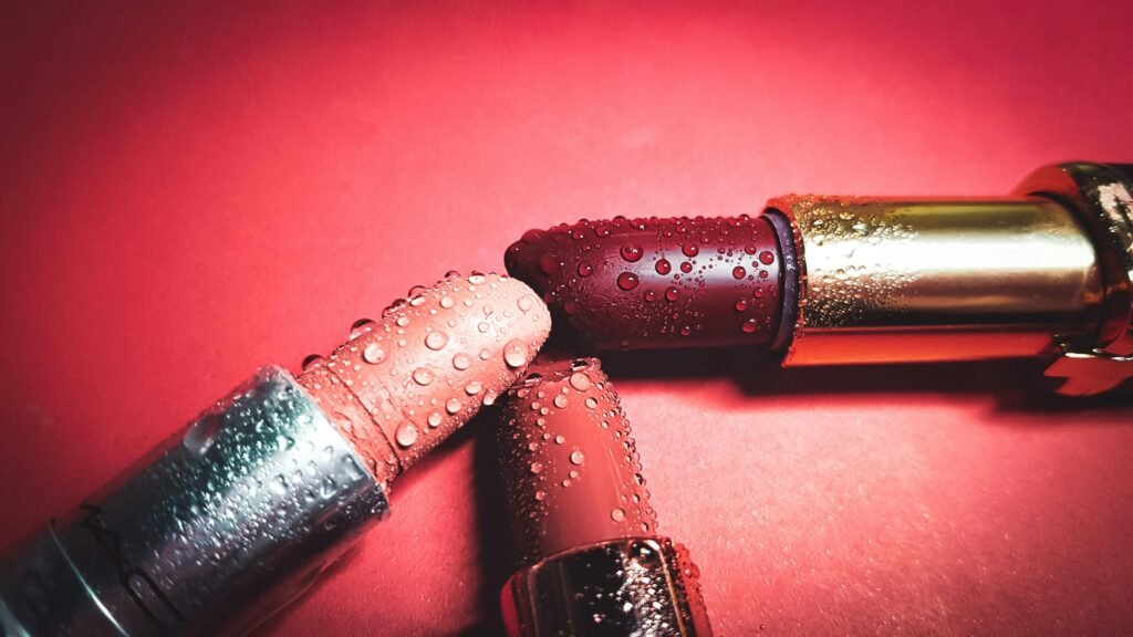 Close-up of colorful lipsticks with water droplets on a pink background, highlighting beauty.